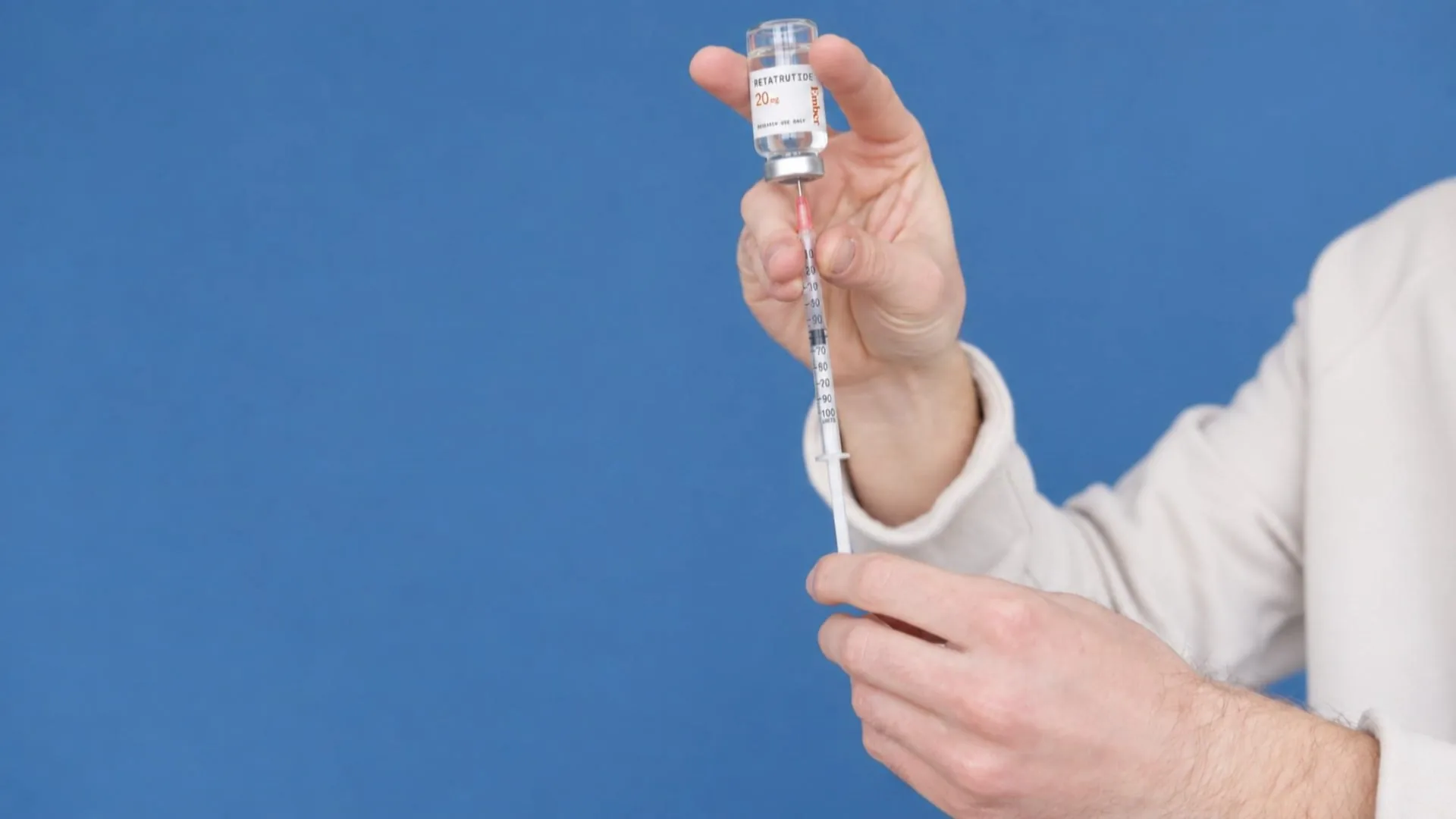 Hands holding a Retatrutide research vial against a blue background